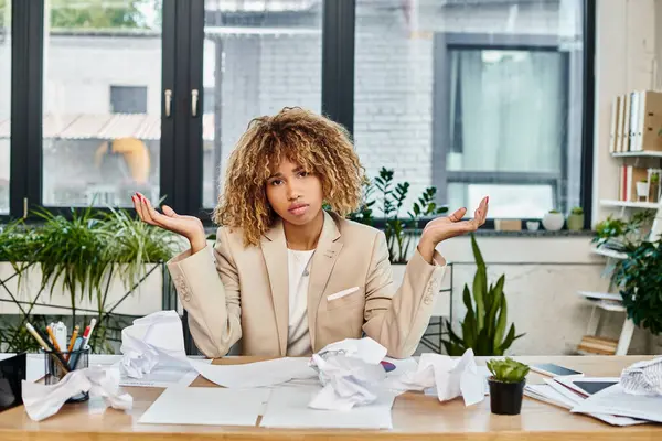 Confused curly african american businesswoman at her desk with crumpled papers, stress at work — Stock Photo