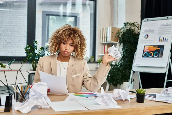 Pensativo rizado africano americano mujer de negocios en su escritorio y la celebración de arrugado papeles, estrés - foto de stock