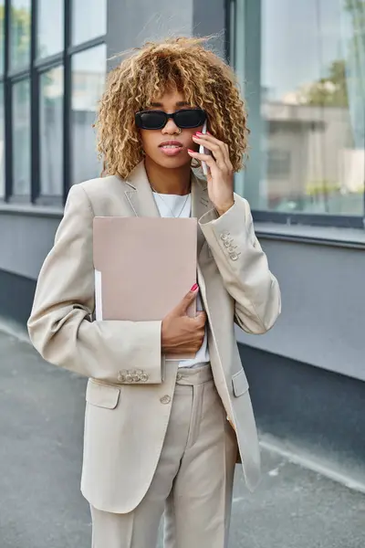 Chic femme afro-américaine en costume et lunettes de soleil passer un appel à l'extérieur d'un immeuble de bureaux — Photo de stock