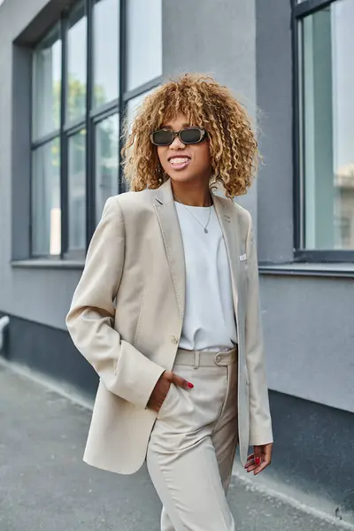 Cheerful african american woman with braces posing in suit and sunglasses near office building — Stock Photo