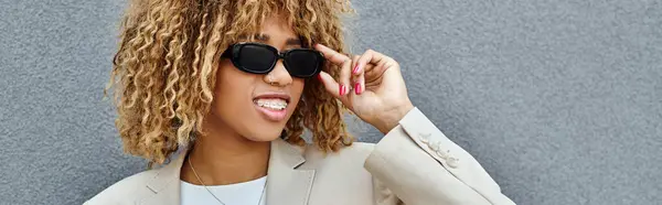 Happy african american woman with braces wearing sunglasses near office building, banner — Stock Photo