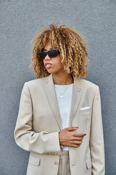 Curly african american woman with braces in suit and sunglasses standing near office building — Stock Photo