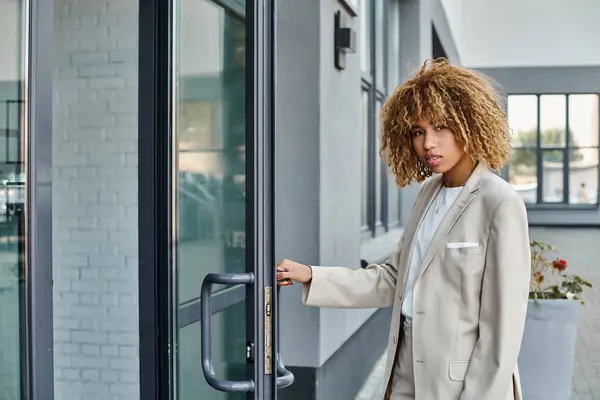 Mujer de negocios afroamericana rizada en ropa formal que entra en el edificio de oficinas, joven profesional - foto de stock
