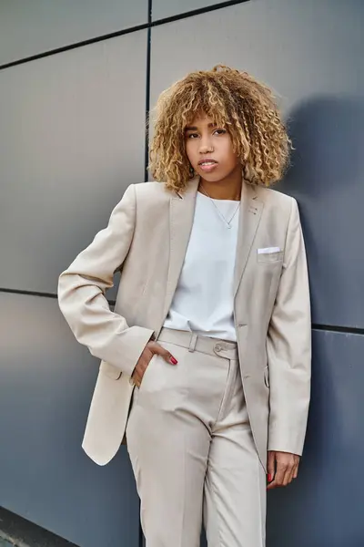 Curly african american businesswoman in suit posing with hand in pocket near office building — Stock Photo