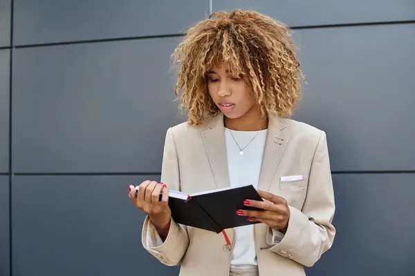 Пенсійна афроамериканська бізнес-леді в офісному одязі, дивлячись на її блокнот біля офісної будівлі — стокове фото