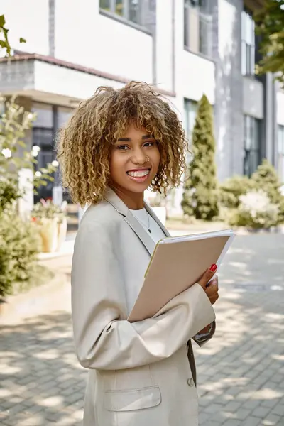 Happy african american entrepreneur in braces standing with folder near office building on sunny day — Stock Photo