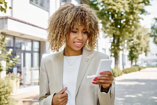 Happy african american businesswoman in braces walking with smartphone near office building — Stock Photo
