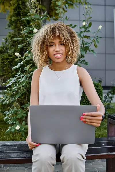 Felice riccio africano americano freelance utilizzando il suo computer portatile e seduto sulla panchina, donna di carriera — Foto stock