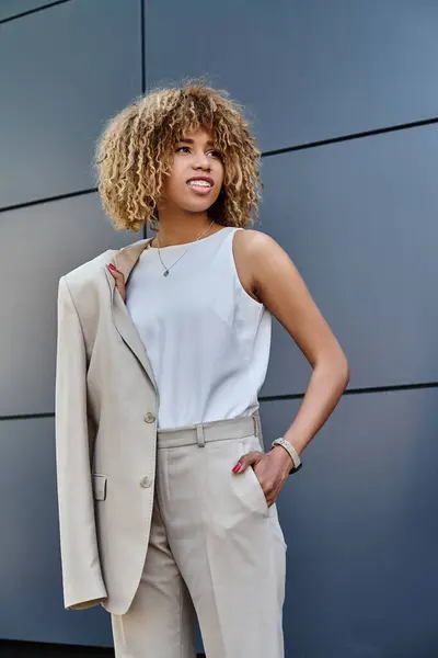 Cheerful and curly african american businesswoman with blazer standing against a modern building — Stock Photo