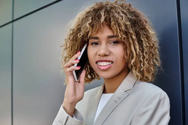 Cheerful and pierced african american businesswoman with curly hair talking on smartphone — Stock Photo