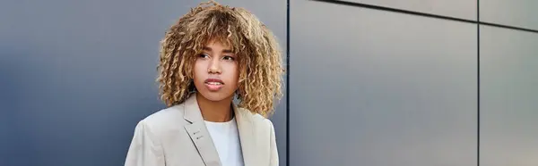 Stylish professional banner, young and curly african american woman sitting by grey office wall — Stock Photo
