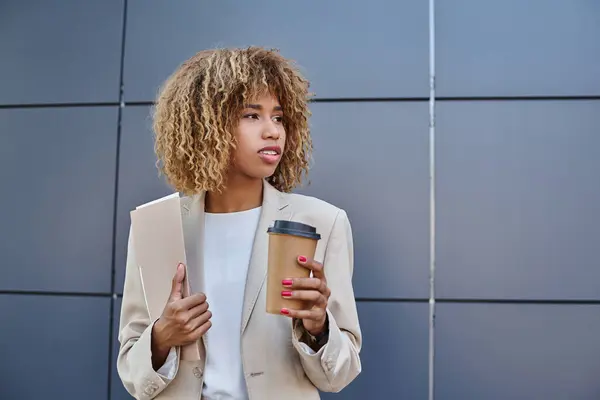 Elegante donna americana africana professionale con caffè e cartellina pieghevole accanto alla parete grigia dell'ufficio — Foto stock