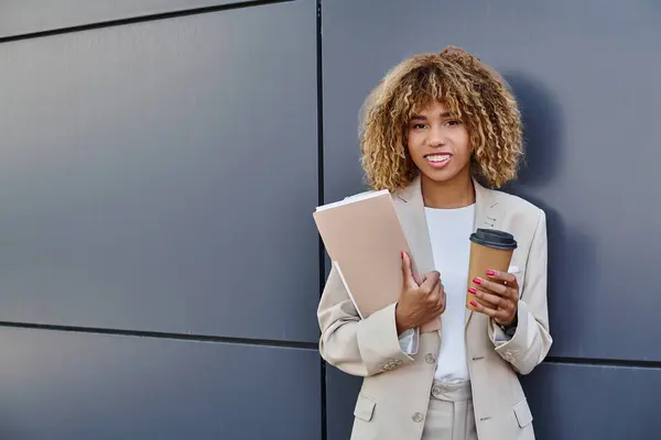 Professional headshot, happy african american woman with coffee and folder standing by office wall — Stock Photo