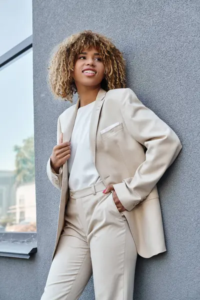 Joven y positiva mujer de negocios afroamericana en ropa formal de pie con la mano en el bolsillo al aire libre - foto de stock