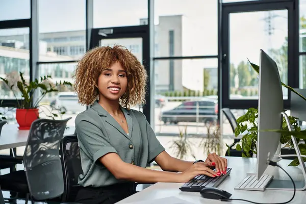 Feliz jovem Africano americano empresária sentado na mesa na frente do monitor de computador no escritório — Fotografia de Stock