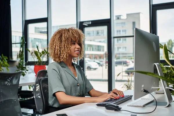 Positif jeune gestionnaire afro-américain travaillant au bureau en face de moniteur d'ordinateur dans le bureau — Photo de stock