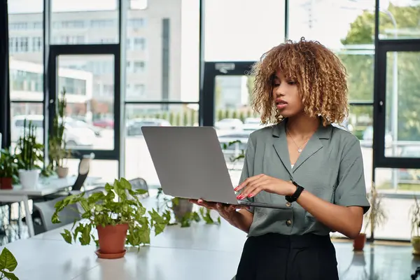 Займається роботою молода афроамериканська бізнес-леді, використовуючи ноутбук, стоячи в добре освітленому офісі — стокове фото