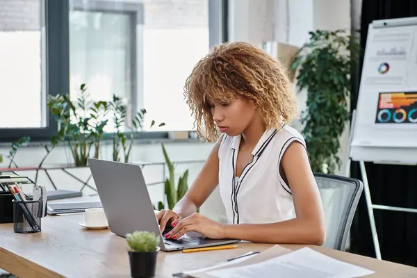 Курчаво-африканская американская деловая женщина в повседневной одежде работает на ноутбуке за столом в современном офисе — стоковое фото