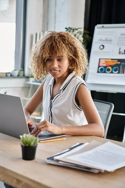Happy african american businesswoman in casual attire working on laptop at desk in modern office — Stock Photo
