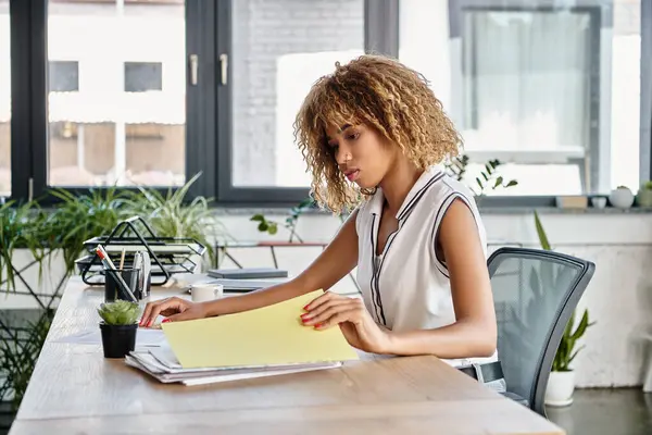 Focused african american businesswoman with curly hair reviewing files at her working desk — Stock Photo