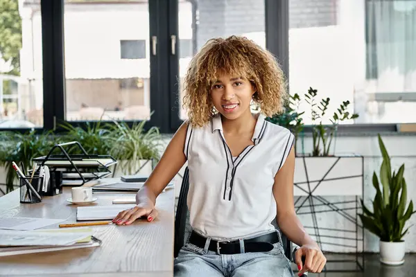 Mulher de negócios americana africana alegre com cabelo encaracolado sentado em sua mesa de trabalho com artigos de papelaria — Fotografia de Stock