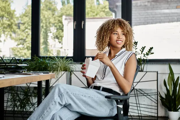 Heureux afro-américain femme tenant baguettes et profiter asiatique emporter repas dans bureau — Photo de stock