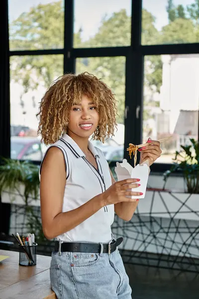Feliz encaracolado Africano americano mulher segurando takeaway refeição na caixa de papelão e olhando para a câmera — Fotografia de Stock