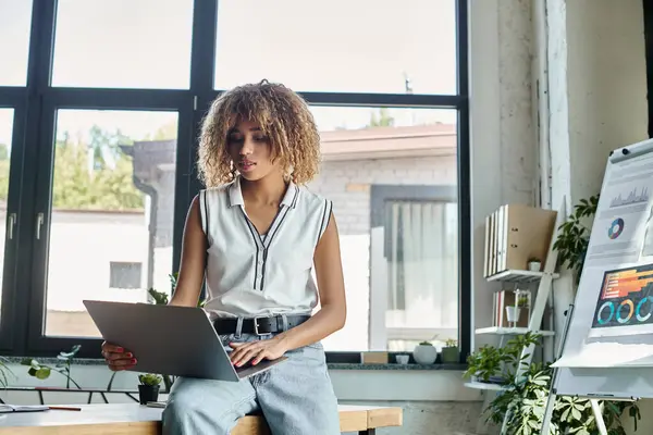 African american businesswoman analyzes data on her laptop in sunlit, plant-filled office — Stock Photo