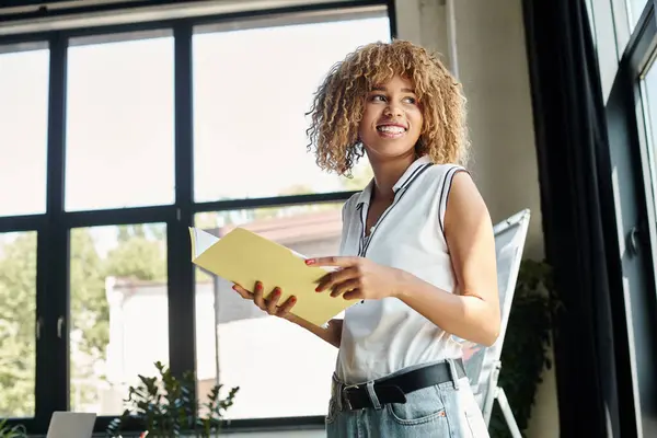 Heureux entrepreneur afro-américain à bretelles tenant des documents dans un espace de travail moderne chic — Photo de stock