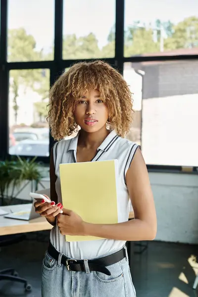 Curly african american entrepreneur in braces holding documents and smartphone in office — Stock Photo