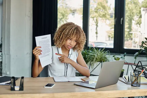 Focalisé afro-américaine femme montrant contrat avec son doigt lors d'un appel vidéo sur ordinateur portable — Photo de stock