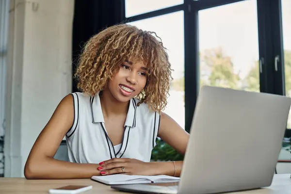 Feliz mujer de negocios afroamericana con una sonrisa amistosa durante la videollamada en el ordenador portátil en la oficina - foto de stock