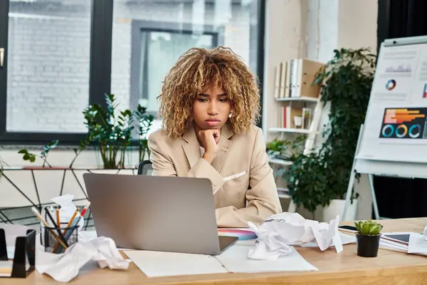 Overwhelmed african american businesswoman looking at laptop around paperwork chaos on desk — Stock Photo