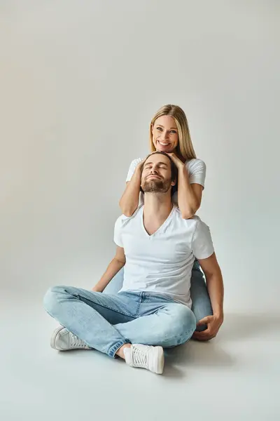 Un hombre se sienta en el suelo mientras la mujer descansa sobre su espalda, mostrando un momento tierno e íntimo entre la sexy pareja. - foto de stock