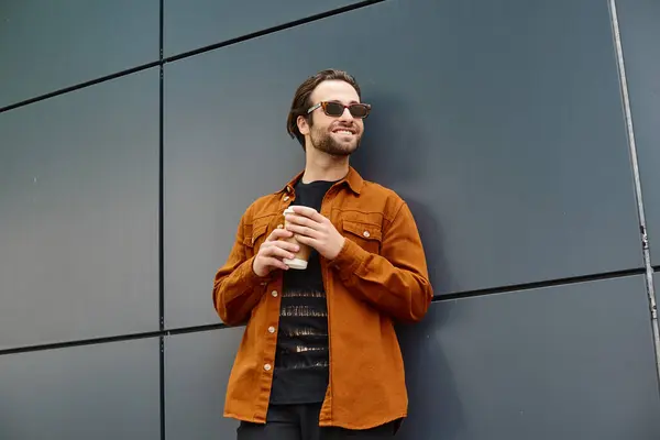 A man leaning against a wall, holding a cup of coffee. — Stock Photo