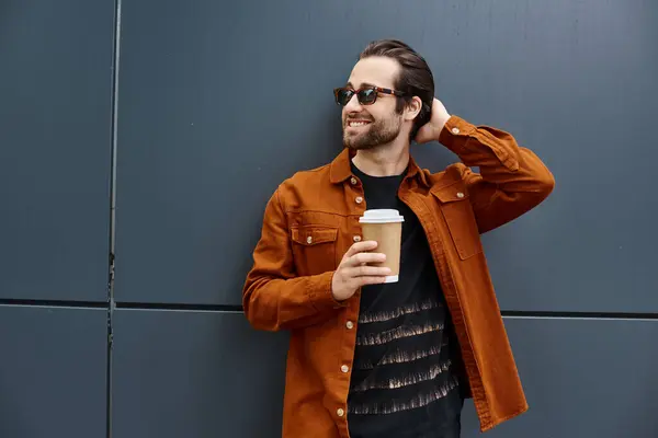 A stylish man in an orange jacket savoring a cup of coffee with a smile on his face. — Stock Photo