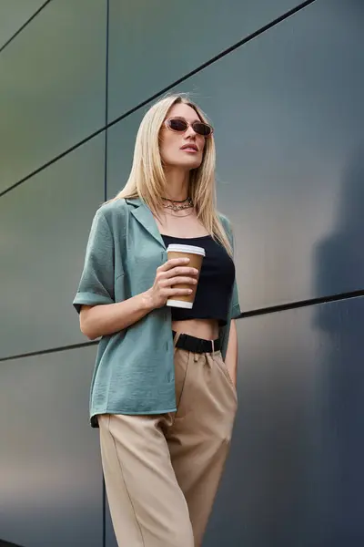 Una donna tiene gioiosamente una tazza di caffè in piedi accanto a un muro, abbracciando la calma della sua routine mattutina.. — Foto stock
