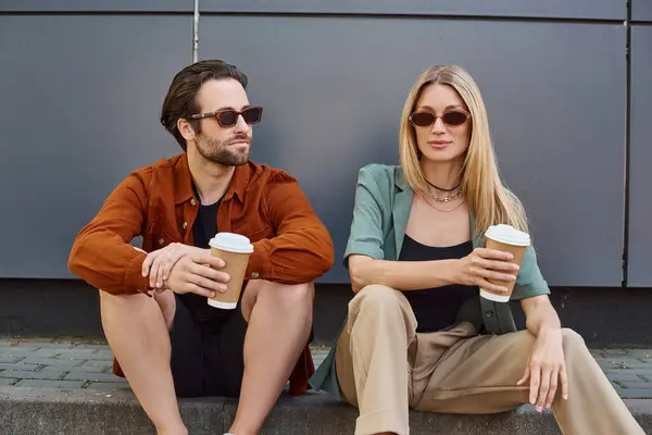 Un hombre y una mujer se sientan cerca, sosteniendo tazas de café, compartiendo un momento de intimidad y conexión. - foto de stock