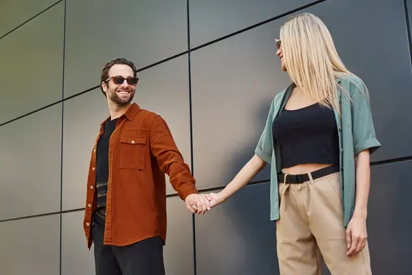 A sexy couple holding hands in front of a wall, displaying romance and connection. — Stock Photo