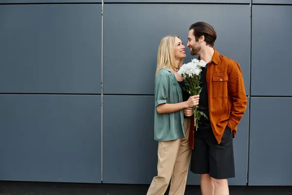 Un hombre y una mujer, exudando encanto, de pie juntos, ella sosteniendo un ramo de flores vibrantes. - foto de stock