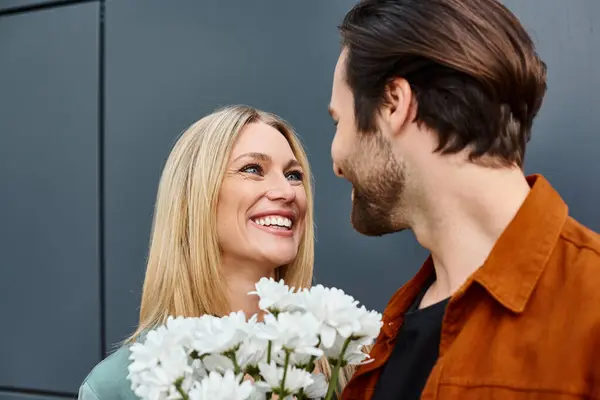 Un hombre de pie junto a una mujer, presentándole un ramo de flores blancas en un gesto romántico. - foto de stock