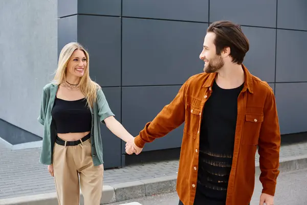 Un homme élégant et une belle femme marchent main dans la main sur une rue urbaine animée, respirant la romance et la connexion. — Photo de stock