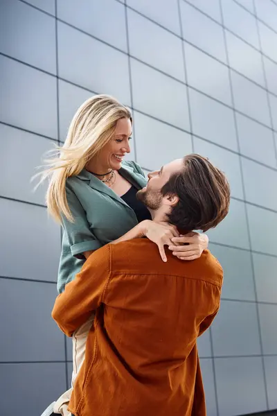 A man holding a woman lovingly in front of a striking urban building, exuding romance and intimacy in the cityscape. — Stock Photo