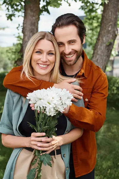 Um homem ternamente detém um buquê de flores ao lado de uma mulher, incorporando um momento romântico e amoroso entre o casal. — Fotografia de Stock