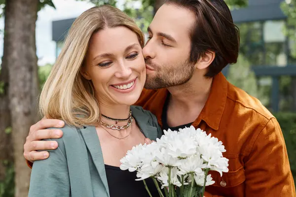 Um homem amoroso beija apaixonadamente uma mulher segurando um belo buquê de flores. — Fotografia de Stock