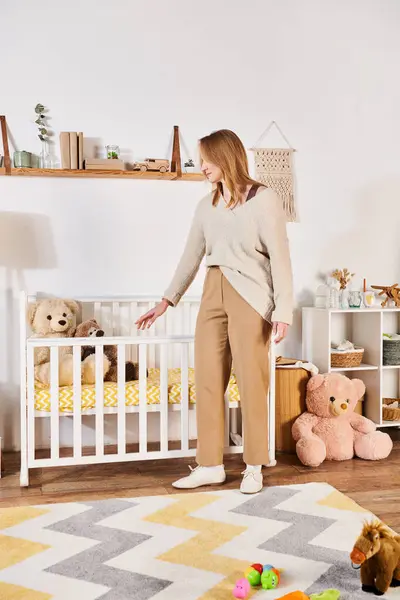 Jovem grávida de pé perto berço em quarto de crianças com brinquedos macios em casa, expectativa de nascimento — Fotografia de Stock