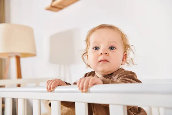 Сладкий ребенок ребенка стоя и глядя прочь в кроватке в детской комнате дома, счастливое детство — стоковое фото