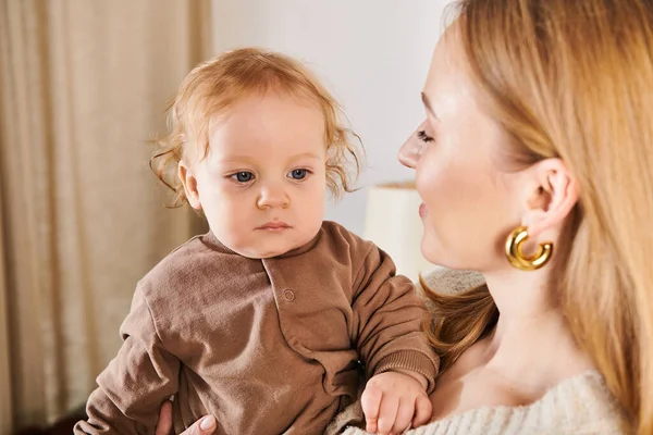 Jeune femme attrayante tenant mignon petit fils dans les mains dans la chambre d'enfant à la maison, maternité heureuse — Photo de stock