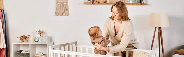 Feliz joven madre sosteniendo lindo toddle hijo cerca cómodo cuna en cuarto de la guardería, pancarta horizontal - foto de stock