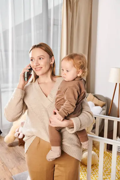Happy woman with cute little son in hands talking on mobile phone at home, multitasking mother — Stock Photo